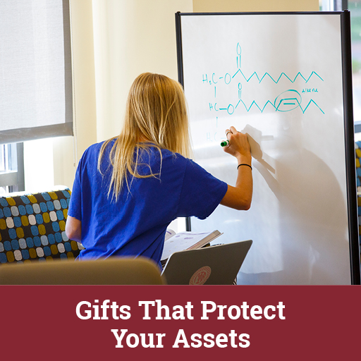 Photo of a student writing on a white board. Links to Gifts That Protect Your Assets